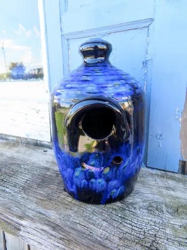 Deep blue glazed ceramic birdhouse jug on a weathered wood surface