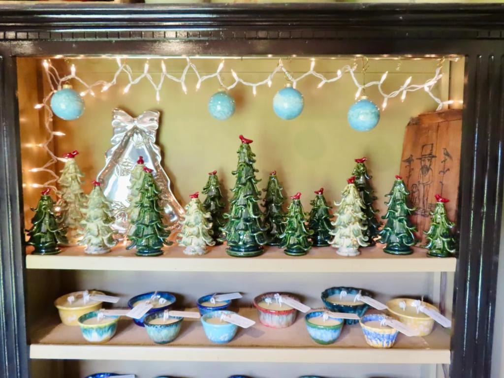 Glazed ceramic Christmas trees and soy candle bowls in a lit display case