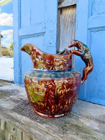 Ornate brown and green glazed ceramic pitcher with decorative handle