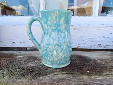 Turquoise crystalline-glazed ceramic pitcher on a weathered wood surface